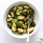 A bowl containing air fried brussels sprouts. A serving spoon rests in the bowl.