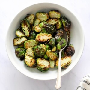 A bowl containing air fried brussels sprouts. A serving spoon rests in the bowl.