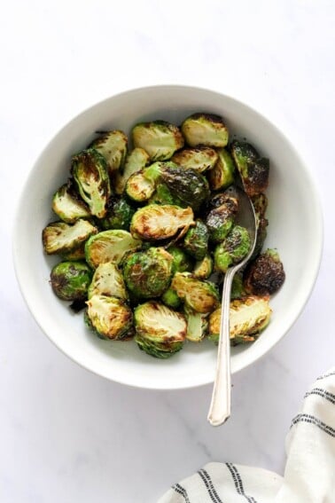 A bowl containing air fried brussels sprouts. A serving spoon rests in the bowl.