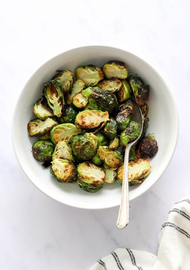 A bowl containing air fried brussels sprouts. A serving spoon rests in the bowl.