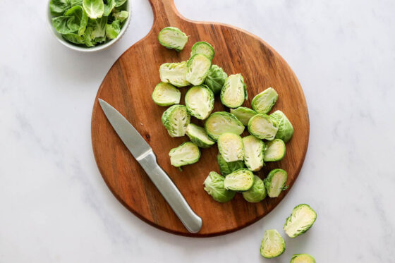 Chopped brussels sprouts on a round wooden cutting board.