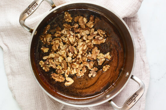 Toasted walnuts added to a sauce pan containing coconut sugar and water mixture.