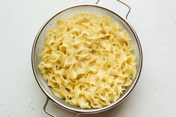 A mesh strainer with cooked chunky noodles after draining.