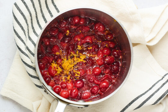 Cooked cranberries in a saucepan with grated orange zest added on top.