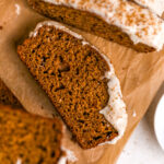 Slices of gingerbread loaf with maple cream cheese frosting on parchment paper.