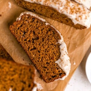 Slices of gingerbread loaf with maple cream cheese frosting on parchment paper.