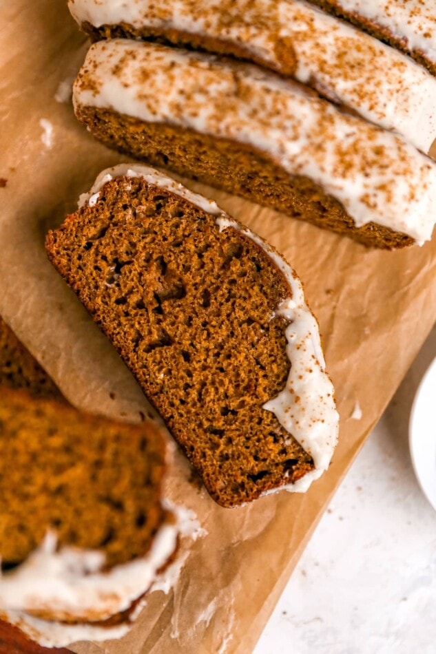 Slices of gingerbread loaf with maple cream cheese frosting on parchment paper.