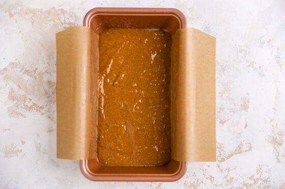 A bread pan with gingerbread loaf batter. The bread pan is lined with parchment paper.