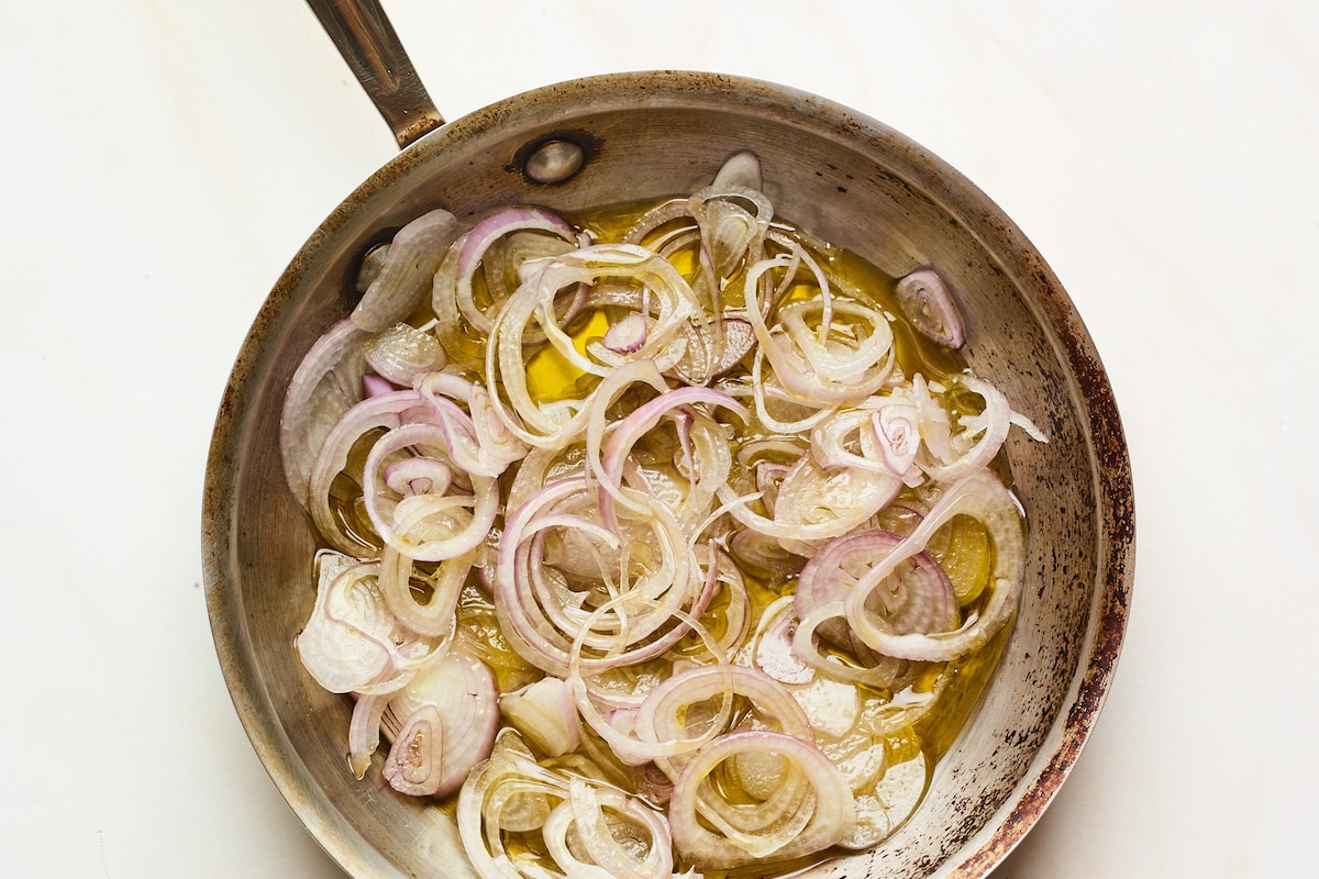 Sliced shallots in oil in a frying pan.