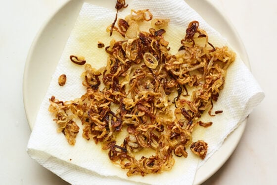Crispy fried shallots on a paper towel, releasing excess oil.
