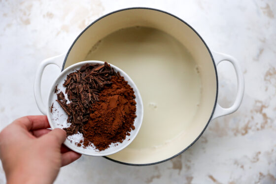 A sauce pan with milk. Cocoa is being added into the sauce pan.