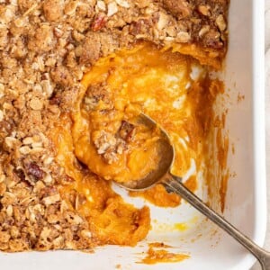 A serving spoon resting in a white baking dish containing sweet potato casserole.