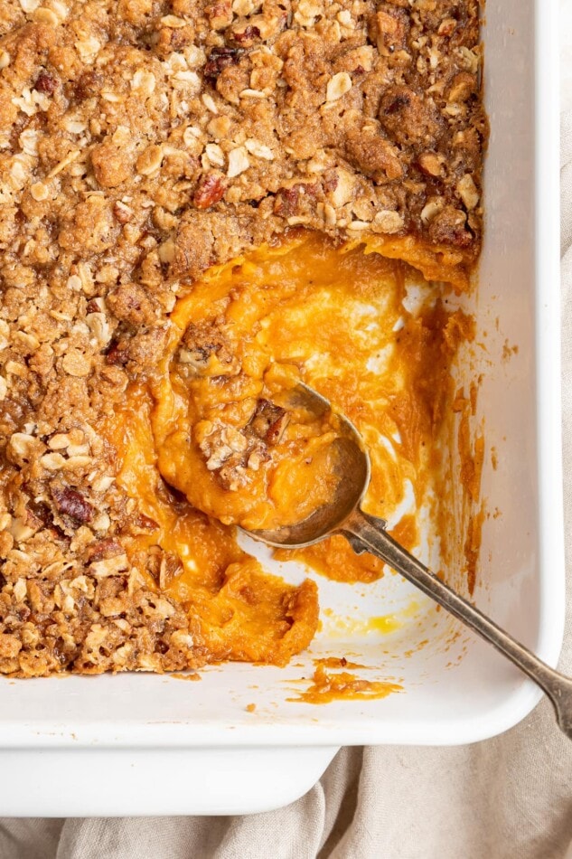 A serving spoon resting in a white baking dish containing sweet potato casserole.