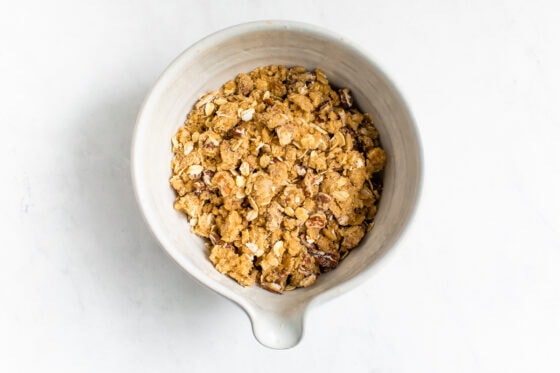 A ceramic mixing bowl containing oats, brown sugar, pecans, oat flour and coconut oil mixed together to make a topping for casserole.