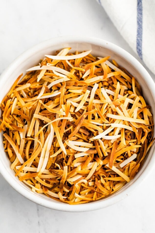 A closeup overhead photo looking at a bowl containing toasted shredded coconut.