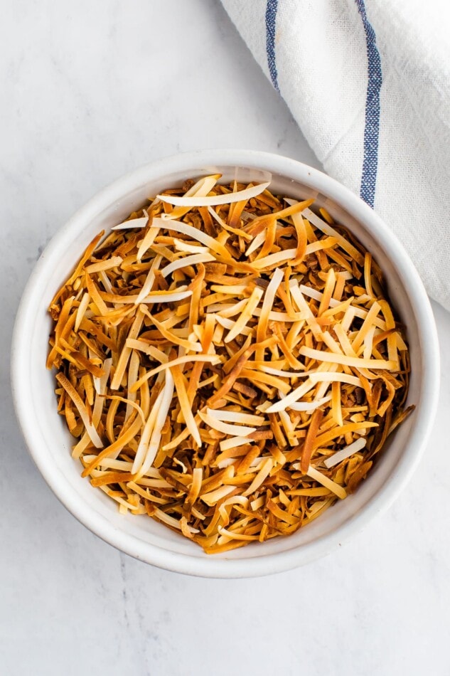 An overhead photo looking at a bowl containing toasted shredded coconut.