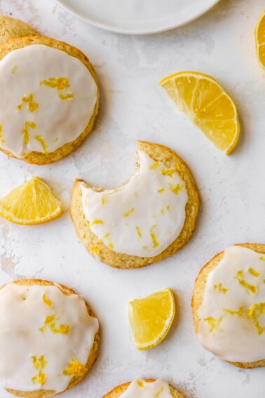 An overhead photo looking at lemon almond flour cookies scattered on a table top. The center cookie has a bite removed.