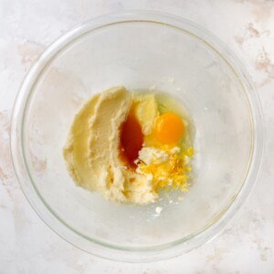 Vanilla, lemon extract, egg, lemon zest, and lemon juice added to a mixing bowl containing creamed butter and sugar.