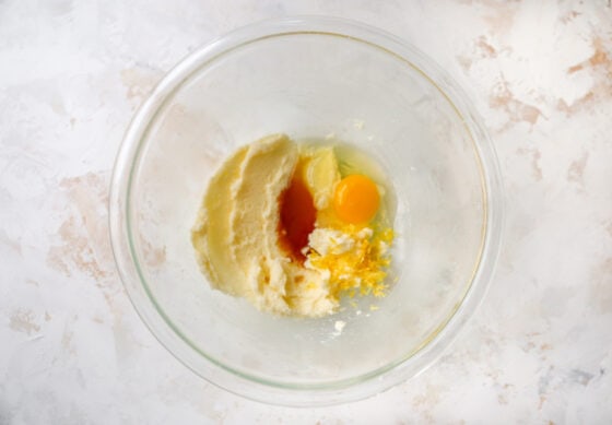 Vanilla, lemon extract, egg, lemon zest, and lemon juice added to a mixing bowl containing creamed butter and sugar.