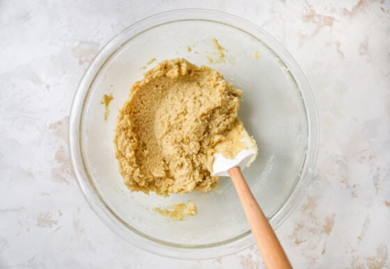 A mixing bowl containing lemon almond flour cookie dough. A spatula rests in the bowl.