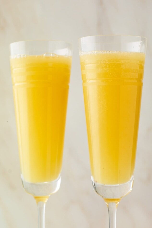A close up of two champagne flutes containing mimosas.
