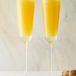 Two champagne flutes containing mimosas.