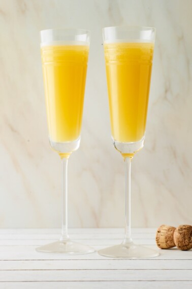 Two champagne flutes containing mimosas.