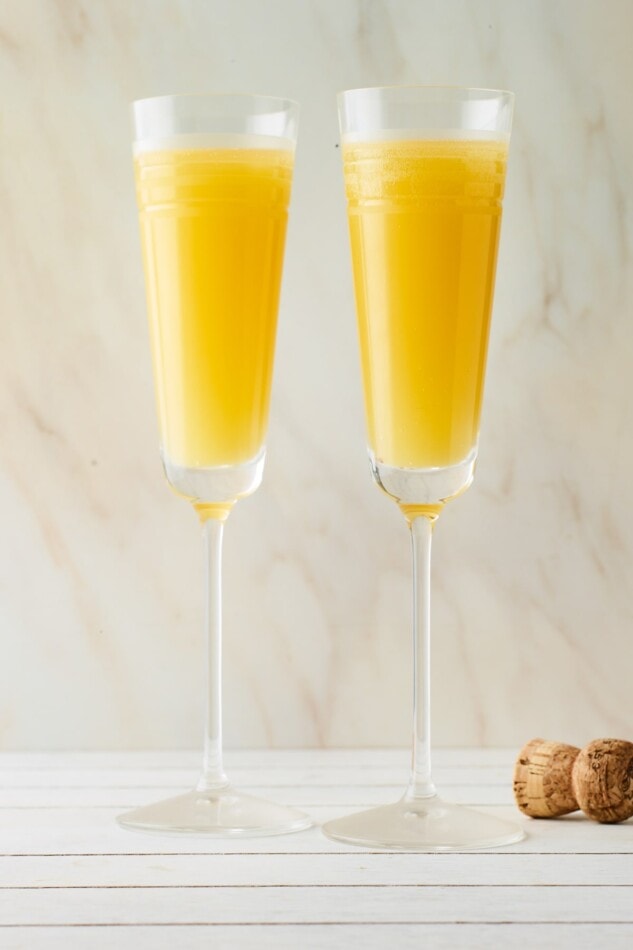 Two champagne flutes containing mimosas.