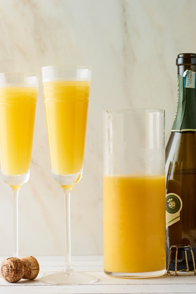 Two Champagne flutes, a bottle of Champagne and a carafe of orange juice. The Champagne flutes have been filled with two-thirds of Champagne and one-third of orange juice.