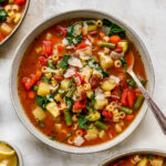 An overhead photo looking at a bowl of minestrone soup. There are two additional bowls cut out of the frame.