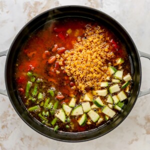 Additional minestrone soup ingredients added to a large pot, including green beans, zucchini, kidney beans and pasta.