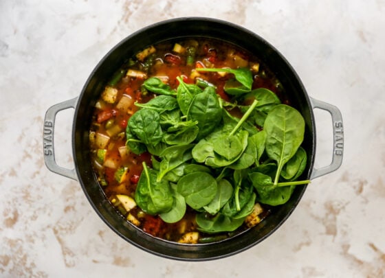 Spinach added to a large pot containing ingredients for minestrone soup.
