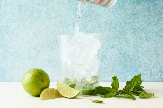 Vodka being poured into a glass with muddled lime and mint.