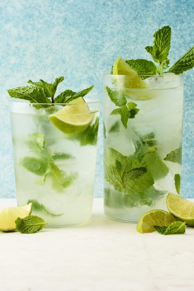 Two glasses containing skinny mojitos. Each glass has sprigs of extra mint and lime wedges.