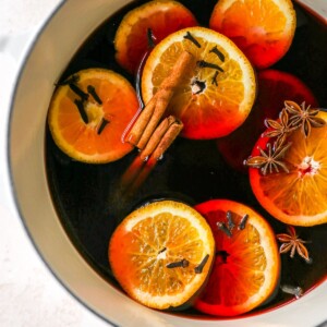 A large pot containing mulled wine with orange slices, cinnamon sticks, cloves and star anise floating in the wine.