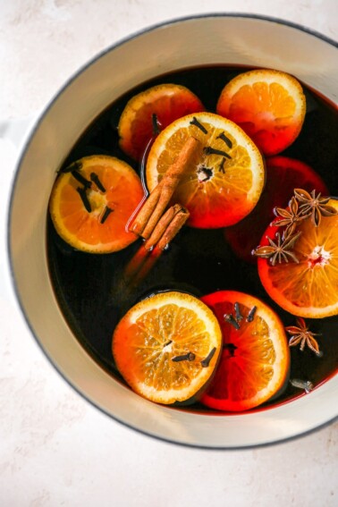 A large pot containing mulled wine with orange slices, cinnamon sticks, cloves and star anise floating in the wine.