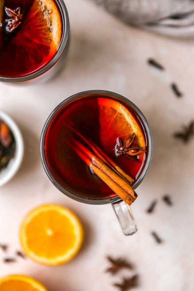 An overhead view of a mug of mulled wine. It is served with a cinnamon stick, orange slice and star anise.