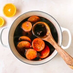 A large pot containing mulled wine, with orange slices floating in the liquid. A wooden spoon is resting inside the pot.