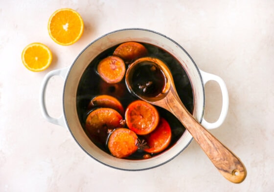 A large pot containing mulled wine, with orange slices floating in the liquid. A wooden spoon is resting inside the pot.