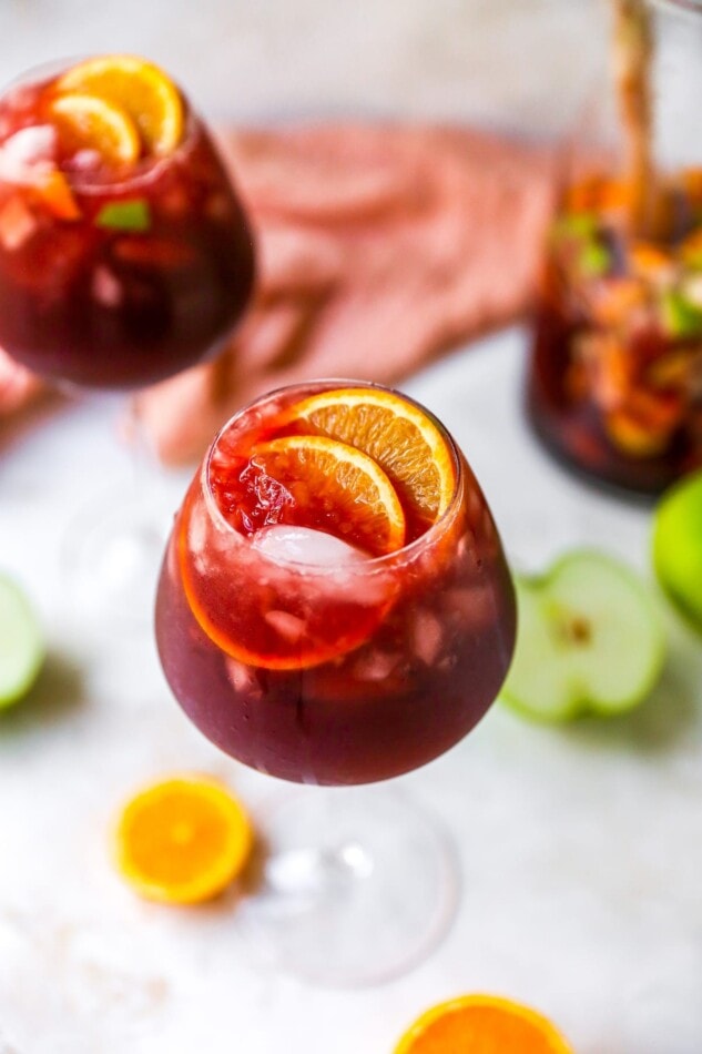 A wine glass containing red wine sangria garnished with two orange slices.