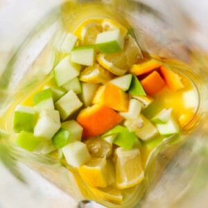 An overhead view of chopped apple, orange and lemon in orange juice in a pitcher.
