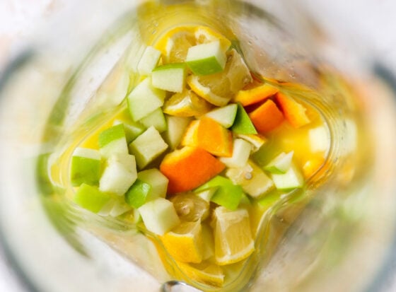 An overhead view of chopped apple, orange and lemon in orange juice in a pitcher.