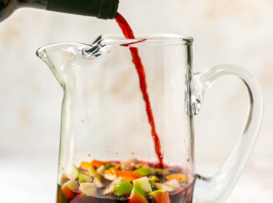 Red wine being poured into a pitcher containing chopped apple, orange and lemon in orange juice.