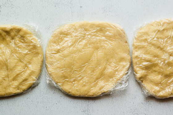 Three discs of rugelach dough wrapped in plastic wrap.