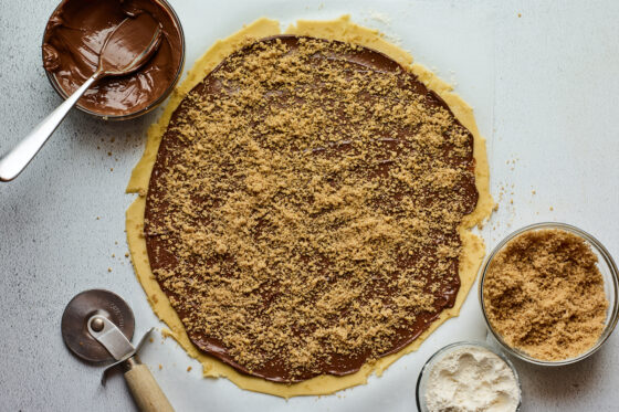 Rugelach dough rolled out into a circle, topped with nutella spread and walnut mixture.