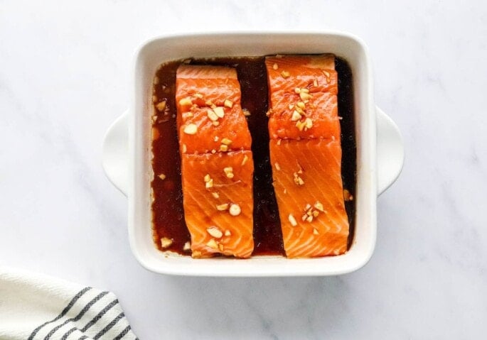 A small baking dish containing 2 salmon filets resting in teriyaki marinade.