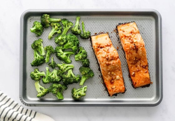 A baking sheet with two freshly baked teriyaki salmon filets on one side and roasted broccoli on the other