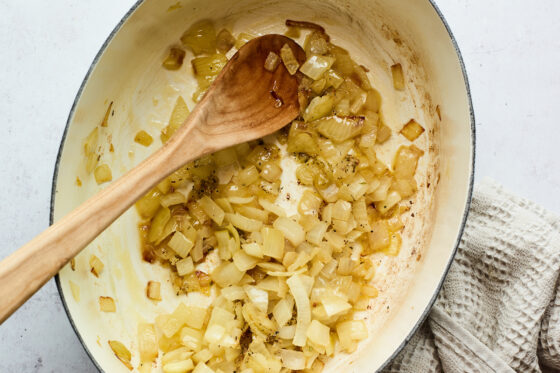 Onions sautéing in a dutch oven. A wooden spoon is resting in the pot.