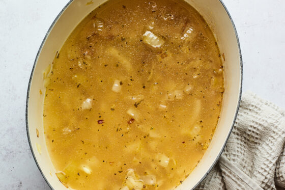 Vegetable broth added to a dutch oven with caramelized onions.