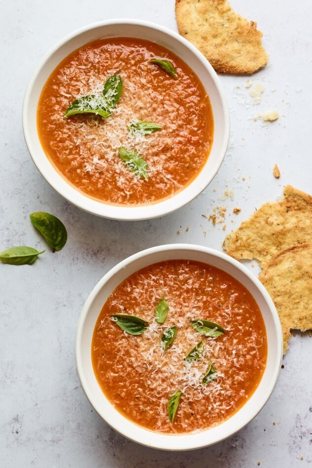 Two bowls containing tomato basil soup. Each bowl is topped with fresh basil leaves.